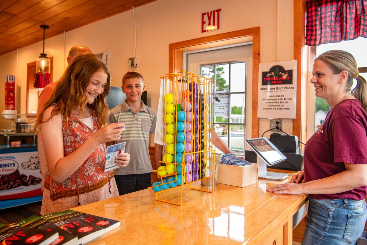 A boy and girl get a brochure from an attendant at a mini golf course. 
